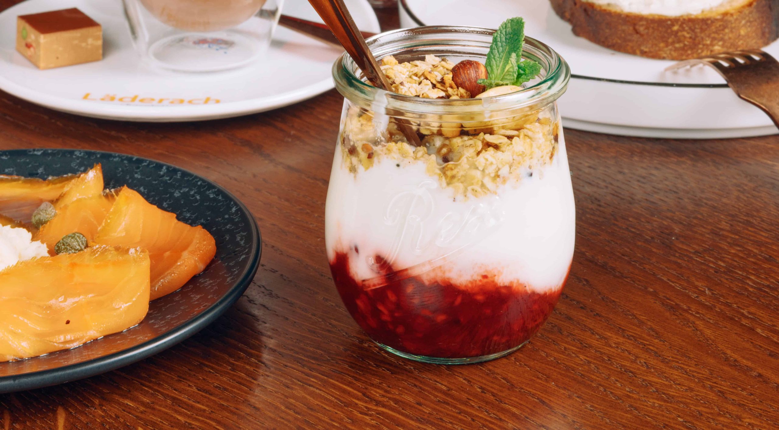 Yogurt parfait with berries, granola, and mint on a wooden table.